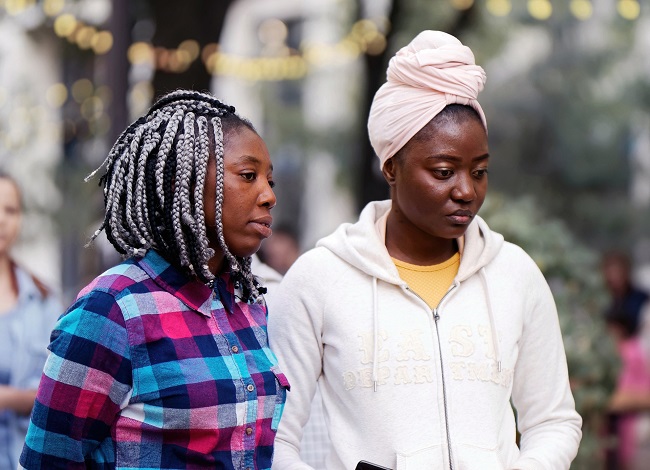 Two women from minority ethnic backgrounds standing next to each other looking downwards.